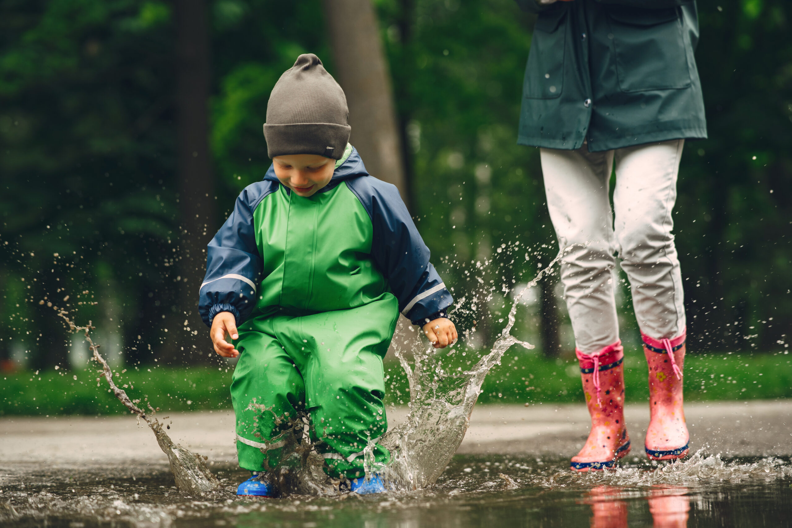 Funny kid in rain boots playing in a rain park
